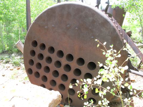 1994 Ford Bronco - A large, circular, rusty metal part with numerous holes, likely from a boiler, sits outdoors amidst foliage.