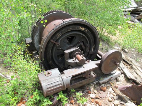 1994 Ford Bronco - An old, large industrial winch mechanism sits abandoned and overgrown in a wooded area.