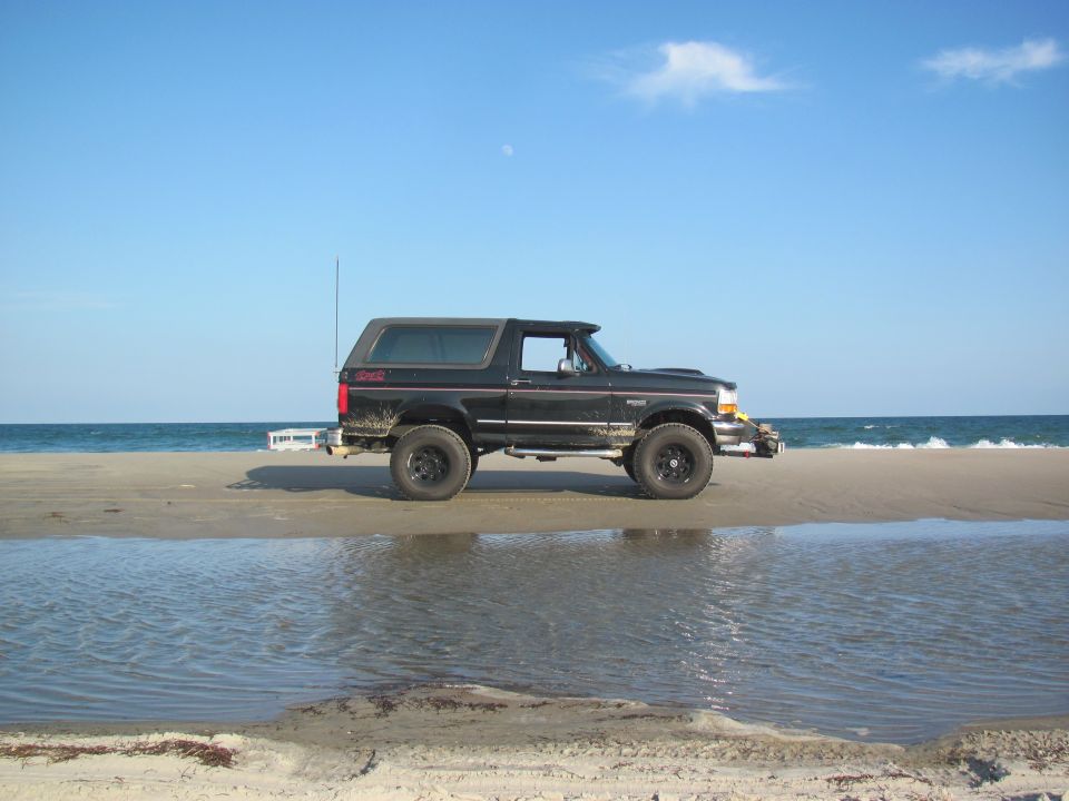 Black Ford Bronco parked on a beach with the ocean in the background