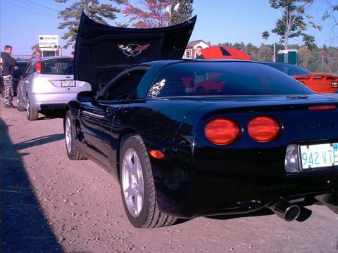 2000 Ford Crown Victoria - A black Chevrolet Corvette is parked with its hood open, alongside other vehicles at an outdoor event.