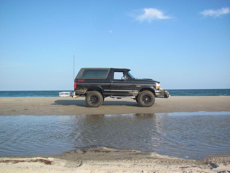 Black Ford Bronco parked on a sandy beach with the ocean in the background
