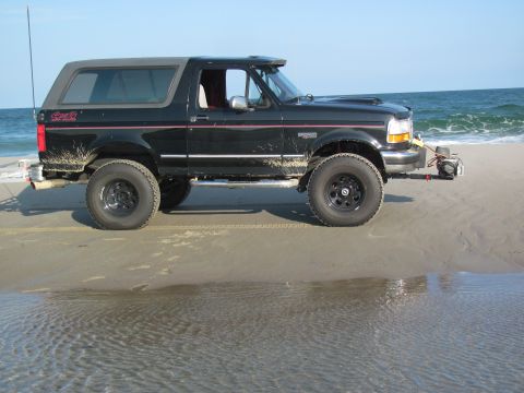 1995 Ford Bronco - A black SUV is parked on the sand near the ocean waves.