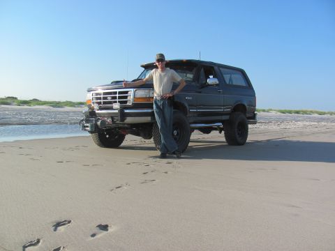 1995 Ford Bronco - A person poses with a black 1995 Ford Bronco on a beach, with the ocean in the background.