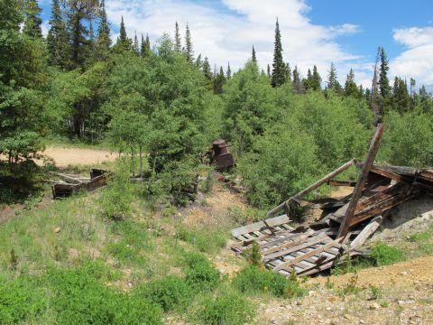 1994 Ford Bronco - Remnants of an old mine sit amongst trees and overgrown vegetation under a partly cloudy sky.