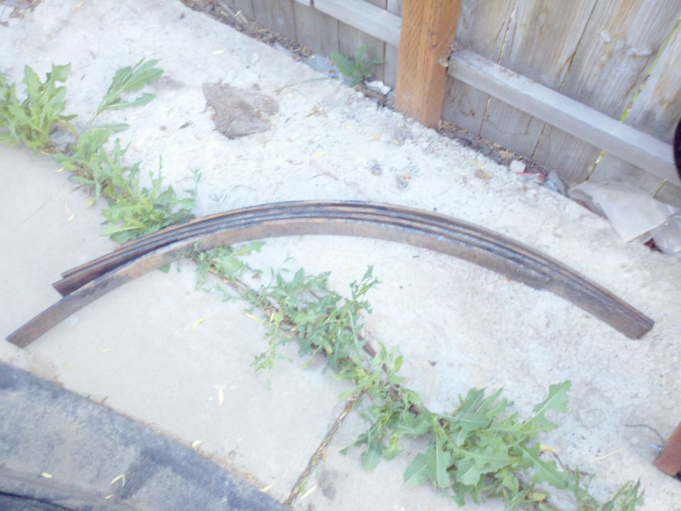 leaf spring lying on concrete near a wooden fence