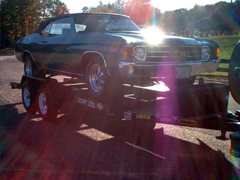 2000 Ford Crown Victoria - A dark green convertible, possibly a 1970 model, is being transported on a trailer under a bright sun.