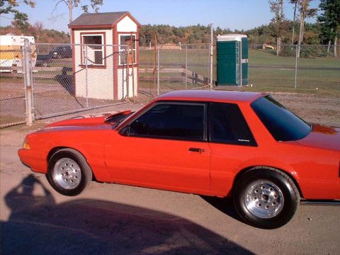 2000 Ford Crown Victoria - A red coupe with a hood scoop and aftermarket wheels is parked at a drag strip.