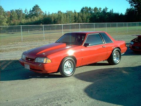2000 Ford Crown Victoria - Red coupe with a prominent hood scoop and drag wheels sits on pavement, with another vehicle partially visible to the right.