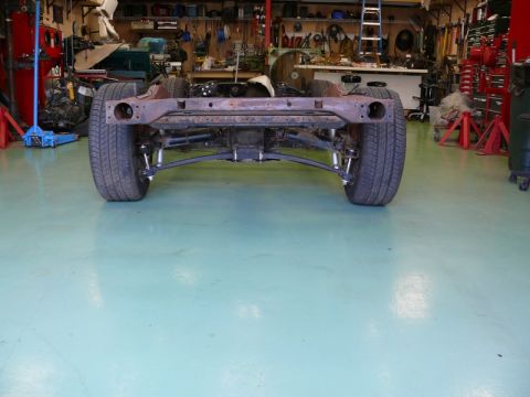 1976 Chevrolet Corvette - Car frame and suspension assembly with rear wheels, viewed from the back in a garage.