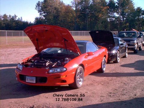 2000 Ford Crown Victoria - A line of cars, including a red Chevrolet Camaro SS, are parked with their hoods open on a dirt lot.