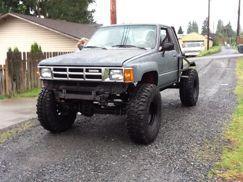 1988 Suzuki Samurai - A modified Toyota pickup truck with oversized tires sits on a gravel road.