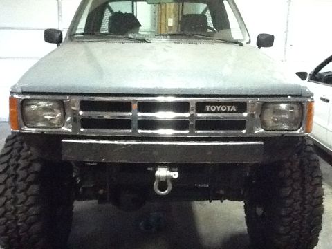 1988 Suzuki Samurai - This 1988 Toyota truck features a prominent chrome grille with the Toyota badge and is equipped with oversized off-road tires.