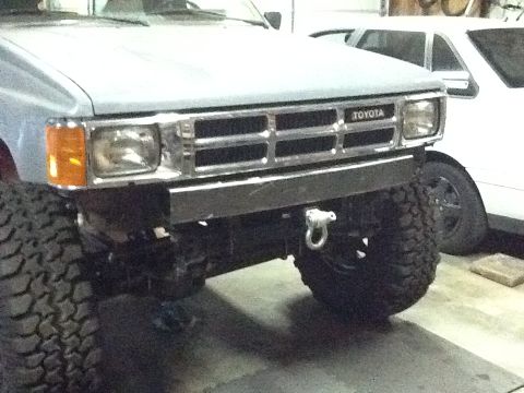 1988 Suzuki Samurai - Front view of a Toyota truck with a custom bumper and off-road tires; a second vehicle is parked behind.