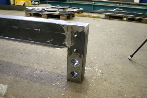 1973 Ford Ranchero - A metal beam with visible welds and drilled holes sits on a concrete floor in a workshop.