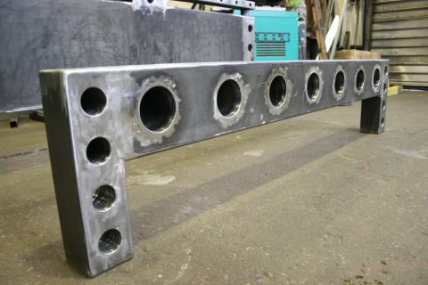 1973 Ford Ranchero - A fabricated metal bracket with numerous holes is shown in a workshop setting.