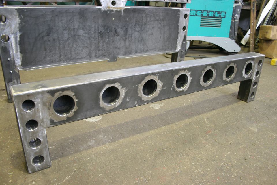 fabricated metal frame with multiple circular cutouts and holes, a teal machine in background