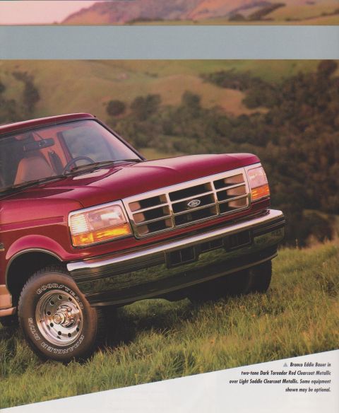 1996 Ford Bronco - A two-tone dark red over light saddle Ford Bronco SUV shown at a 3/4 front angle, parked on a grassy hillside. It has a chrome grille with…