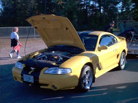 2000 Ford Crown Victoria - A yellow Ford Mustang with black racing stripes is parked with its hood open, revealing the engine bay.