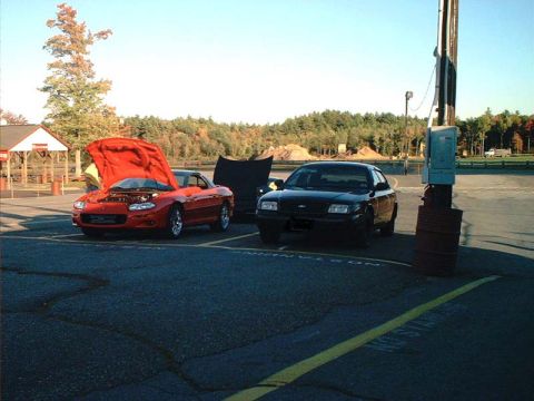 2000 Ford Crown Victoria - A black sedan, possibly a Ford Crown Victoria, is parked with its hood open next to a red sports car.