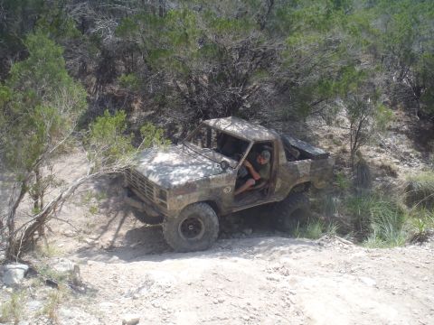 1979 Ford Bronco - A driver maneuvers an off-road vehicle through a challenging, natural terrain with dense foliage.