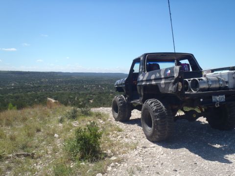 1979 Ford Bronco - This heavily modified SUV, likely a 1978 model, sits on a rocky incline overlooking a wooded valley.