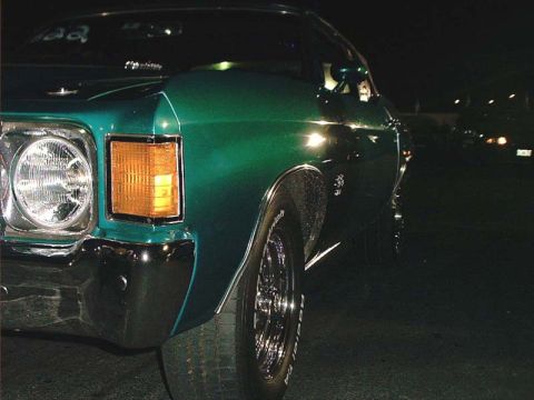 2000 Ford Crown Victoria - A green sedan from the 1970s is viewed from the front corner at night, with a visible tire and chrome bumper.