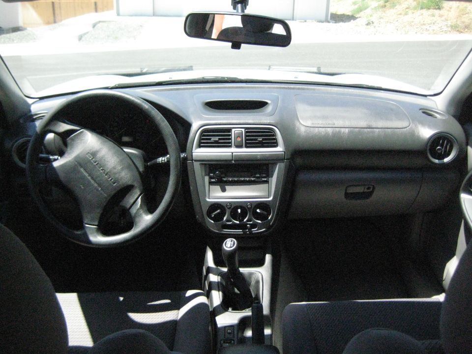 Car interior showing dashboard, steering wheel with Subaru logo, and manual gear shifter
