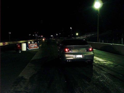 2000 Ford Crown Victoria - A silver sedan is positioned on a drag strip at night, illuminated by track lights.