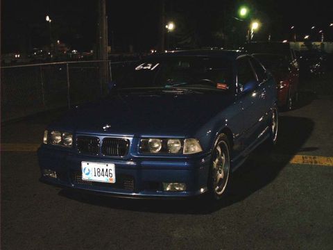 2000 Ford Crown Victoria - A blue BMW E36 coupe is parked at a drag strip at night, with other vehicles visible in the background.