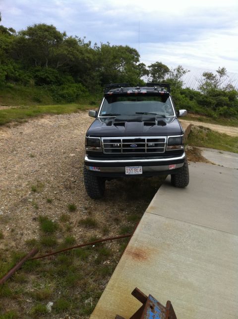 1993 Ford Bronco - A lifted black Ford Bronco is parked on a concrete ramp with a dirt path and vegetation in the background.