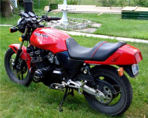 2008 Ford Crown Victoria - A red Suzuki motorcycle is shown from the side, parked on a grassy lawn with a fountain in the background.