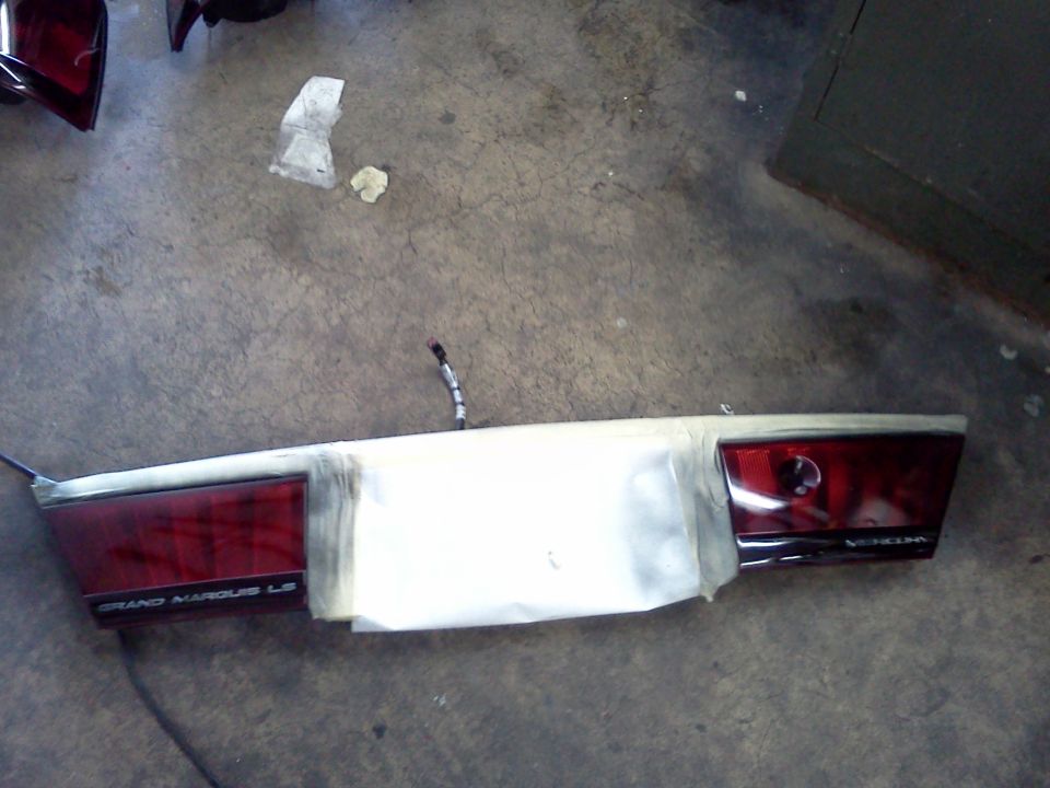 Red car tail light assembly with 'GRAND MARQUIS LS' text, taped in the middle, on a concrete floor