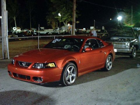2000 Ford Crown Victoria - Orange Ford Mustang at a drag strip at night, with a black pickup truck behind it.