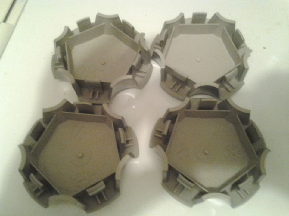 Four tan plastic hubcaps with a pentagonal center and a toothed outer edge
