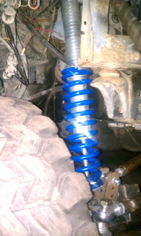 1990 Ford Bronco - Close-up of a blue coilover shock absorber and a large tire, with visible wiring and suspension components.