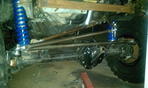 1990 Ford Bronco - Close-up of a modified off-road vehicle's front axle and suspension system with custom linkages and bright blue shocks.