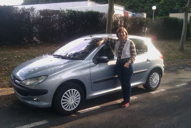Woman leaning on a silver Peugeot 206 hatchback parked on a street