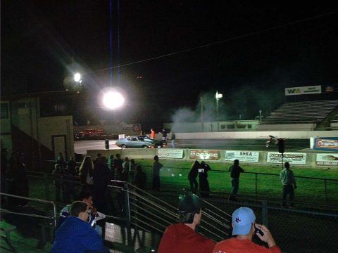 2000 Ford Crown Victoria - A light blue sedan is on the drag strip, with spectators in the foreground and stadium seating in the background.