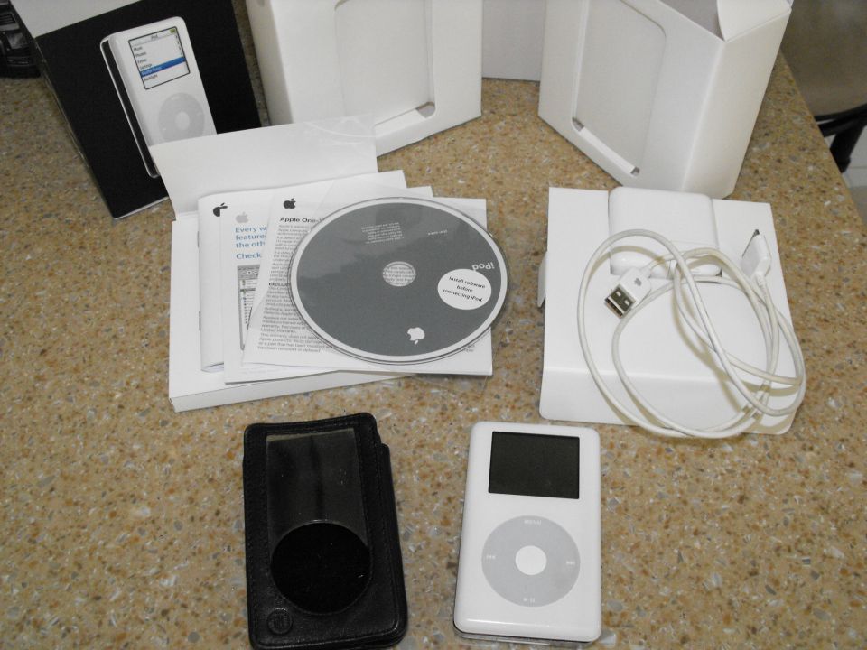 Apple iPod, software disc, charging cable, and manual laid out on a speckled surface