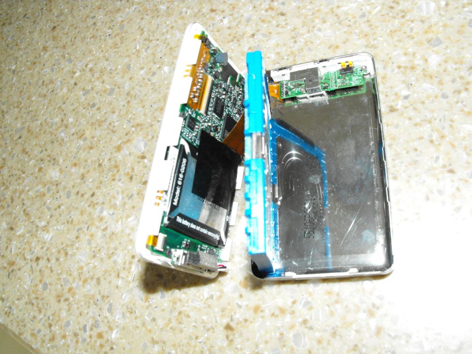 Disassembled electronic device with circuit boards and battery exposed, on a speckled countertop