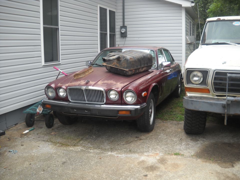 Maroon Jaguar sedan parked next to a white truck, with a fuel tank on its hood