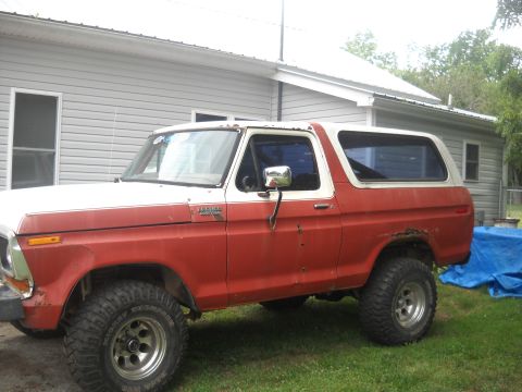 1993 Ford F-150 - This red and white Ford Bronco from the late 1970s is parked in a grassy yard next to a house.