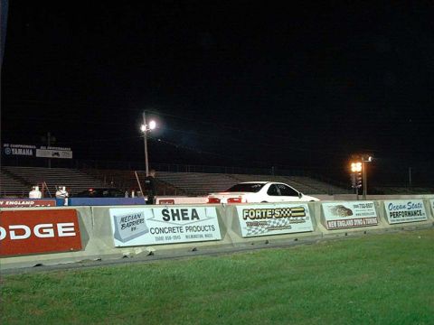 2000 Ford Crown Victoria - A white sedan is positioned on a drag strip at night, with various sponsor advertisements visible on the track barrier.