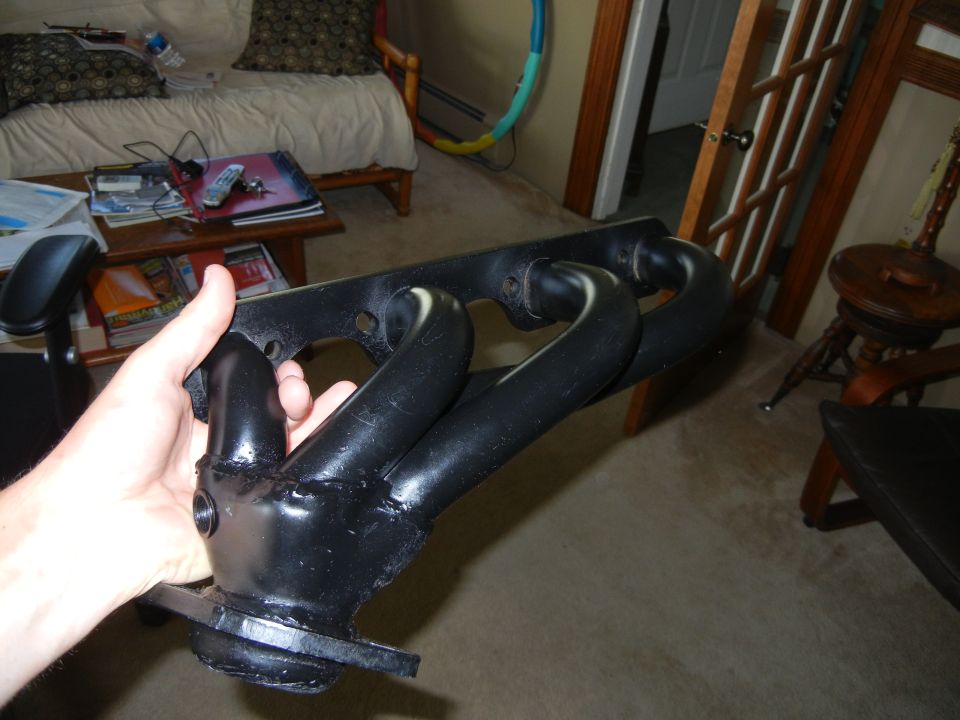 Hand holding black exhaust manifold with four pipes