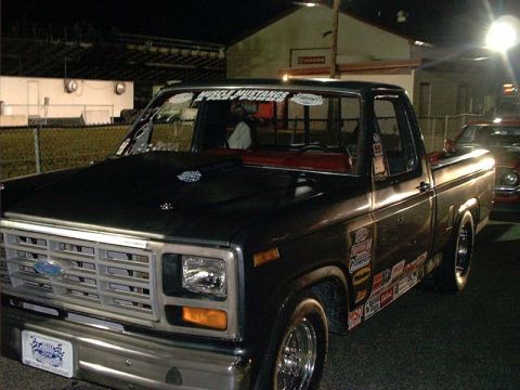 2000 Ford Crown Victoria - A black Ford pickup truck with racing decals is parked at a drag strip.