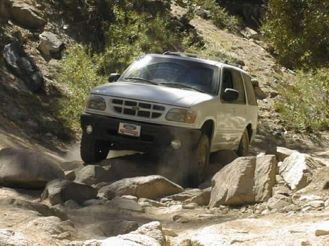 1997 Ford Ranger - Silver/tan Ford Explorer four-door SUV picking its way over large granite boulders on a dusty mountain trail, front three-quarter view show…
