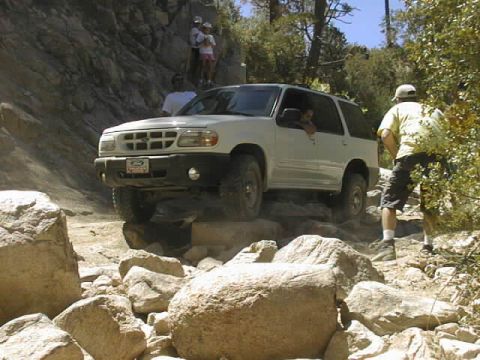 1997 Ford Ranger - White Ford Explorer four-door SUV straddling a granite ledge on a rocky mountain trail with spotters standing alongside and spectators watc…