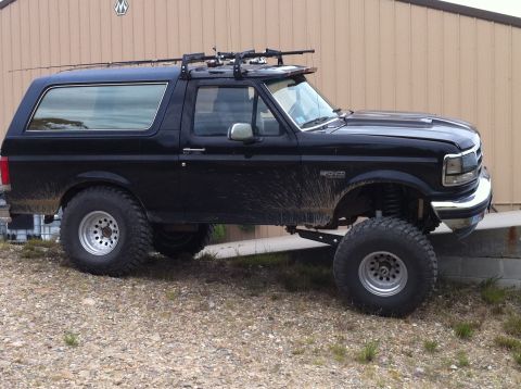 1993 Ford Bronco - Modified 1993 Ford Bronco with off-road tires and roof rack is parked outside a building.