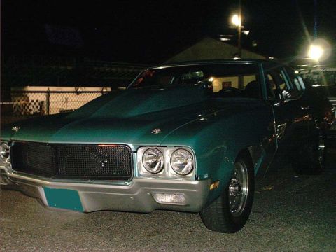 2000 Ford Crown Victoria - teal-green vintage Buick muscle car with dual stacked headlights and mesh grille, parked at night.