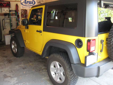 2005 Jeep Wrangler - A yellow Jeep Wrangler with a black hardtop is parked in a garage.